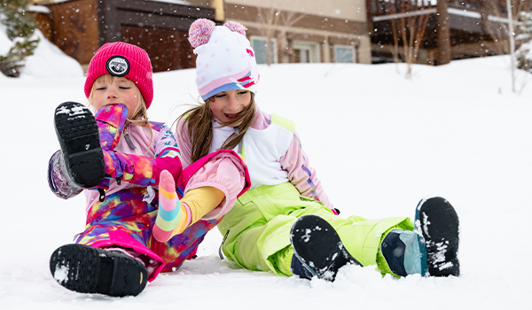 Toddlers wearing snow bibs sitting in the snow.